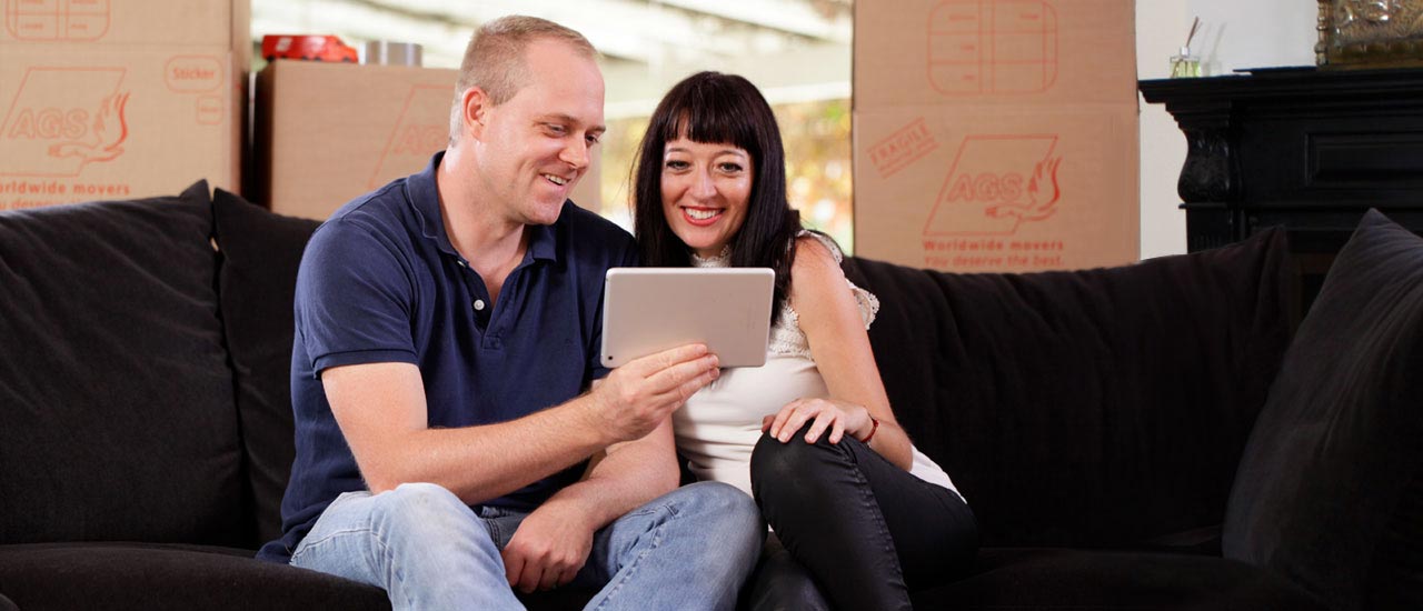 Couple with tablet smiling and sitting on a couch with removal boxes on the back